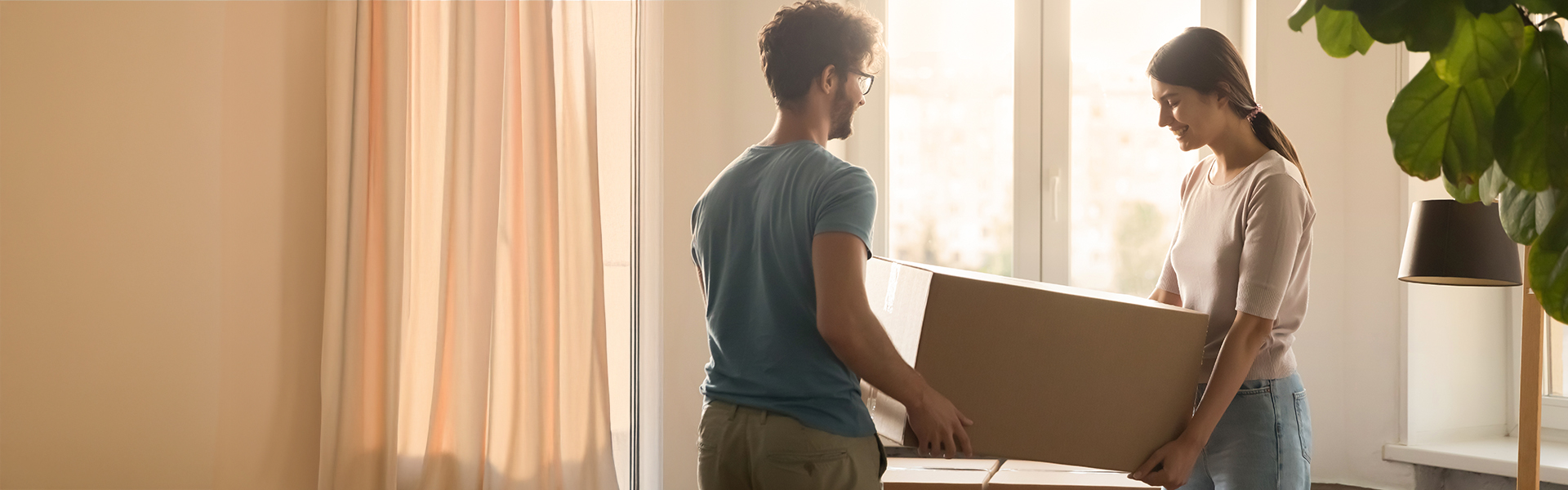 Ein Mann und eine Frau tragen gemeinsam einen Umzugskarton in ihre neuen Wohnung.